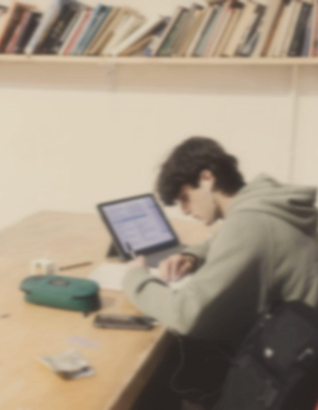 A student with earphones writing notes next to a tablet